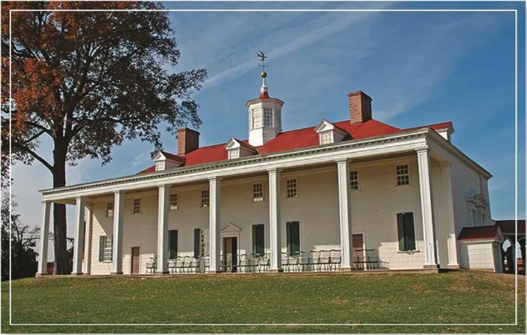 A historical white building with a red roof and surrounding trees under a clear blue sky.
