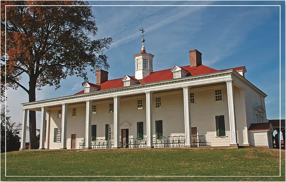 A historical white building with a red roof and surrounding trees under a clear blue sky.